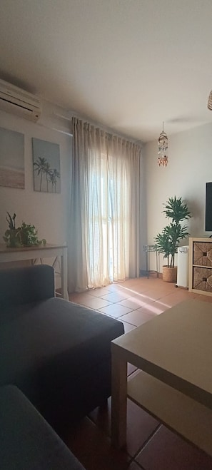 Ein Wohnzimmer mit einer Couch, einem Esstisch, einer Topfpflanze und einem Kronleuchter.