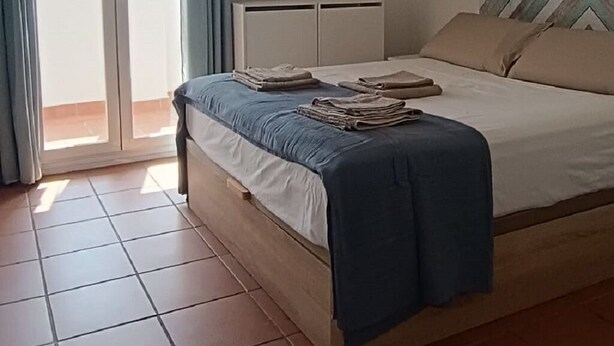 A bedroom with a bed, ceiling fan, air conditioning unit, and a view through a glass door. - Apartment in Conil, located in one of the best areas (Conil de la Frontera)