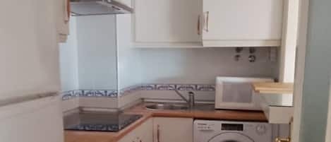 Eine kompakte Küche mit weißen Schränken, einer Waschmaschine, einer Mikrowelle und einem Spülbecken.