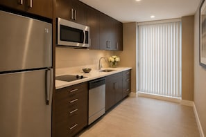 A modern kitchen with stainless steel appliances, a sink, and a window with blinds. - Mayfairs Hotel (Toronto)