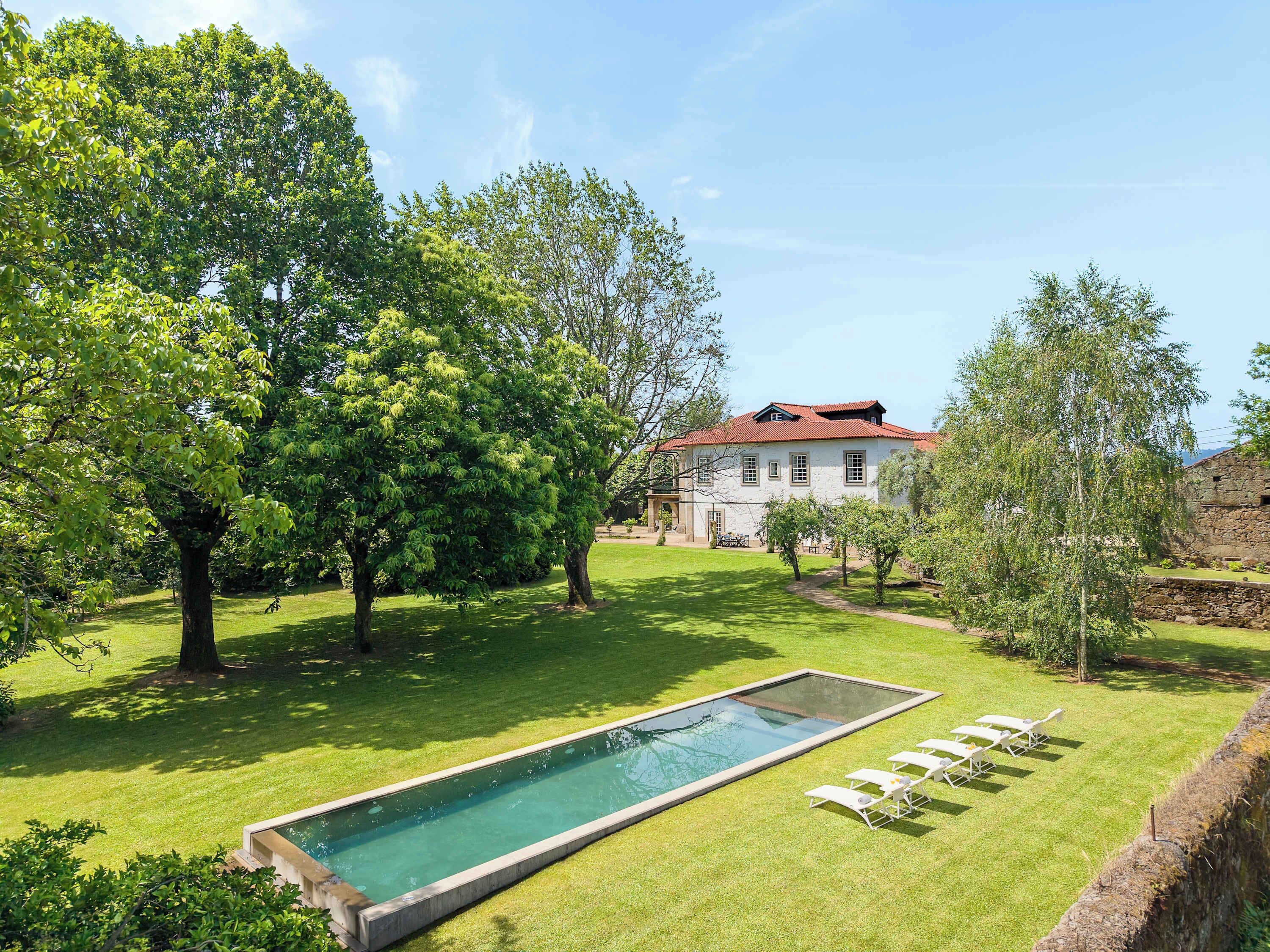 Une piscine entourée de chaises longues, un bâtiment en pierre et une pelouse bien entretenue.
