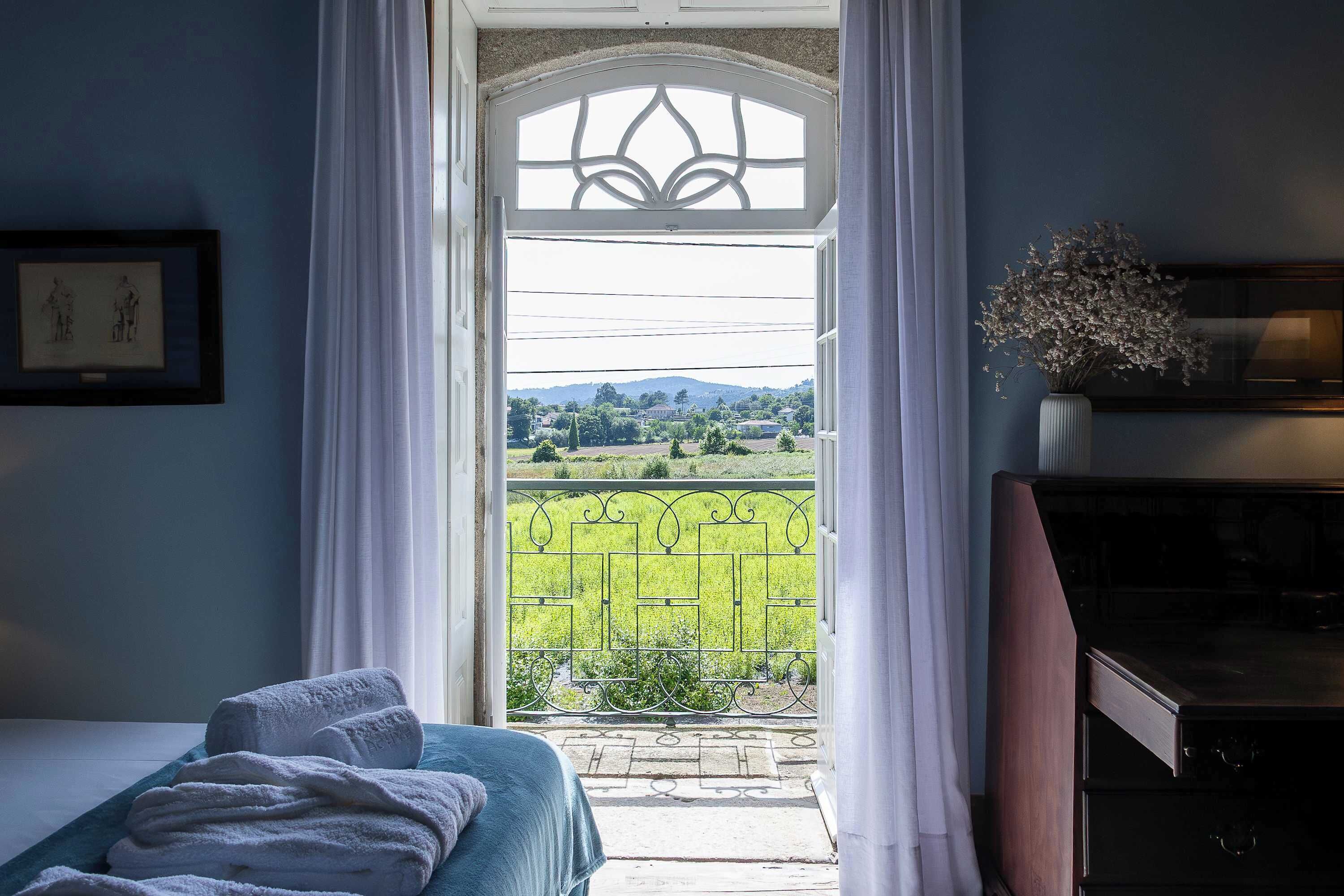 A room with a bed, a desk, and a view of a green landscape through a window.