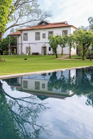 Um edifício grande e branco com telhado de telhas vermelhas, piscina e um gramado bem cuidado.