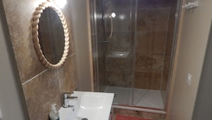 A bathroom with a white sink, a mirror with a rope design, and a glass shower enclosure. - Saint-Malo: Beautiful apartment, 300 m from the train station and Sillon Beach, within the city walls (Saint-Malo)