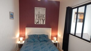A bedroom with a bed, two bedside tables, a nightstand, a wall-mounted poster, and a window with curtains. - Saint-Malo: Beautiful apartment, 300 m from the train station and Sillon Beach, within the city walls (Saint-Malo)