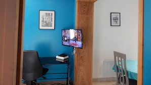 A room with a blue wall, a wooden ceiling, a desk with a chair, a television, and framed pictures. - Saint-Malo: Beautiful apartment, 300 m from the train station and Sillon Beach, within the city walls (Saint-Malo)