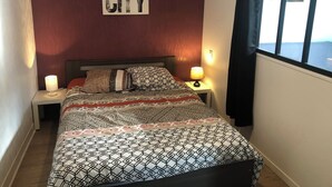 Ein ordentlich bezogenes Bett mit gemusterten Bettwäsche, zwei Nachttischlampen, eine Wanduhr und ein gerahmtes Bild des Empire State Buildings.