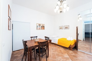 A room with a wooden dining table, four chairs, a bed with a yellow blanket, a chandelier, and two framed pictures on the wall. - Maison Nunzia (Naples)