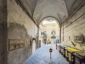 A narrow alleyway with a row of trash bins on one side and a mailbox on the other. - Maison Nunzia (Naples)