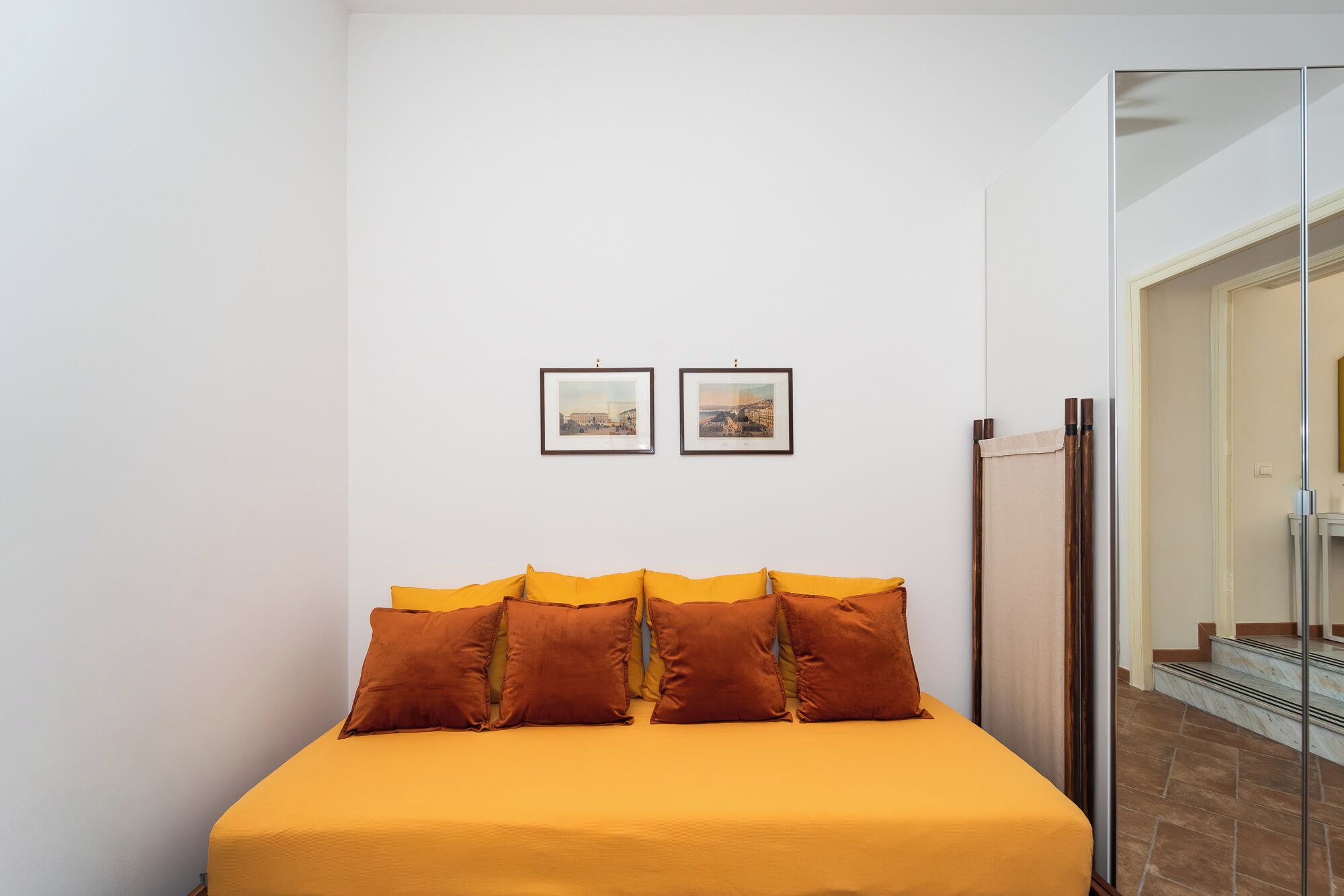 A bedroom with a bed, two framed pictures on the wall, and a mirror.