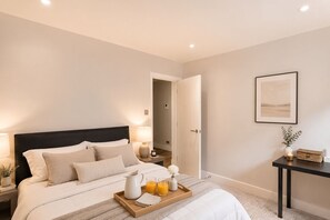 A hotel room with a bed, bedside lamps, a tray with breakfast items, a bedside table with a vase, and a framed picture on the wall. - AC Modern 2 Bed Flat Near St Paul's Cathedral (London)