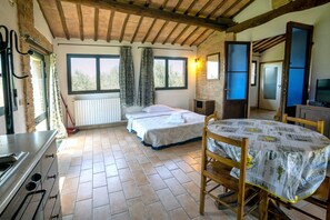 A room with a bed, a table, a kitchen area, and a window with curtains. - Siena Holiday Home With Pool for 4 (Siena)