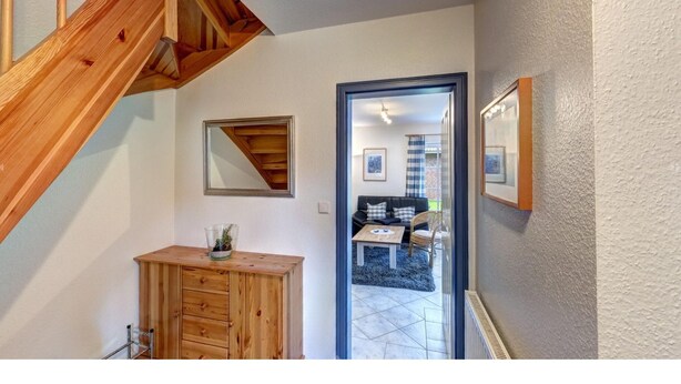 Uma escada de madeira leva a uma sala de estar com sofá, mesa de centro e quadros nas paredes.