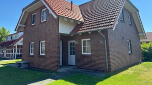 Uma casa de dois andares de tijolo, com telhado de telhas vermelhas, varanda frontal e pequeno jardim da frente.