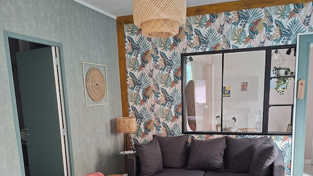 Un soggiorno moderno con un divano componibile, un poggiapiedi rotondo, una lampada a sospensione intrecciata e una carta da parati decorata.