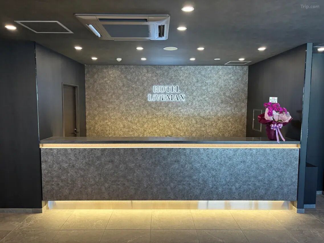 Una recepción con un cartel que dice 'HOTEL LIVEMAX', unidades de aire acondicionado y un arreglo floral.