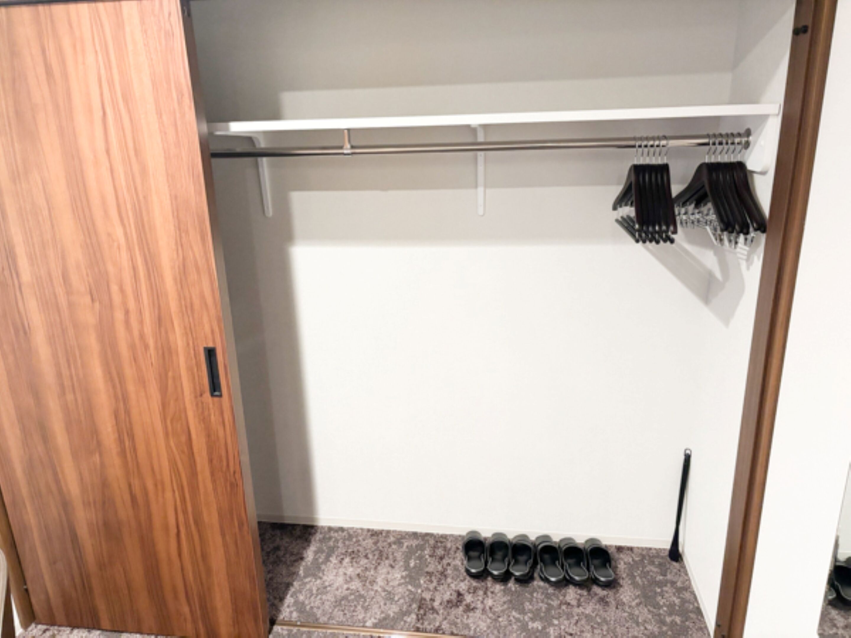 A closet with a wooden door, a shoe rack, and a shoe shelf.