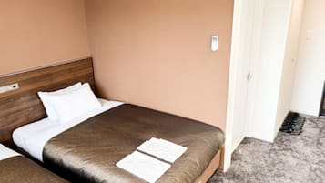 A hotel room with two beds, a wooden headboard, a white door, and a carpeted floor.