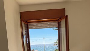 Una stanza con un tavolo e sedie, vista sul mare attraverso una porta aperta e un balcone con ringhiera.