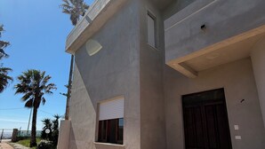 Un edificio moderno con facciata in cemento, una piccola finestra con persiane, una porta in legno scuro e un ingresso pavimentato con gradini.