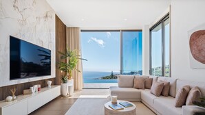 A modern living room with a large TV, a sofa, a coffee table, and a view of the ocean. - Villa Platinum by Homie (Calheta)