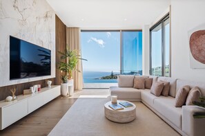 Ein modernes Wohnzimmer mit großem Fernseher, einer Couch, einem Couchtisch und Meerblick.