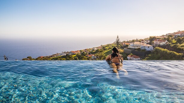 A person in a swimming pool with a view of houses and greenery in the background. - Villa Platinum by Homie (Calheta)