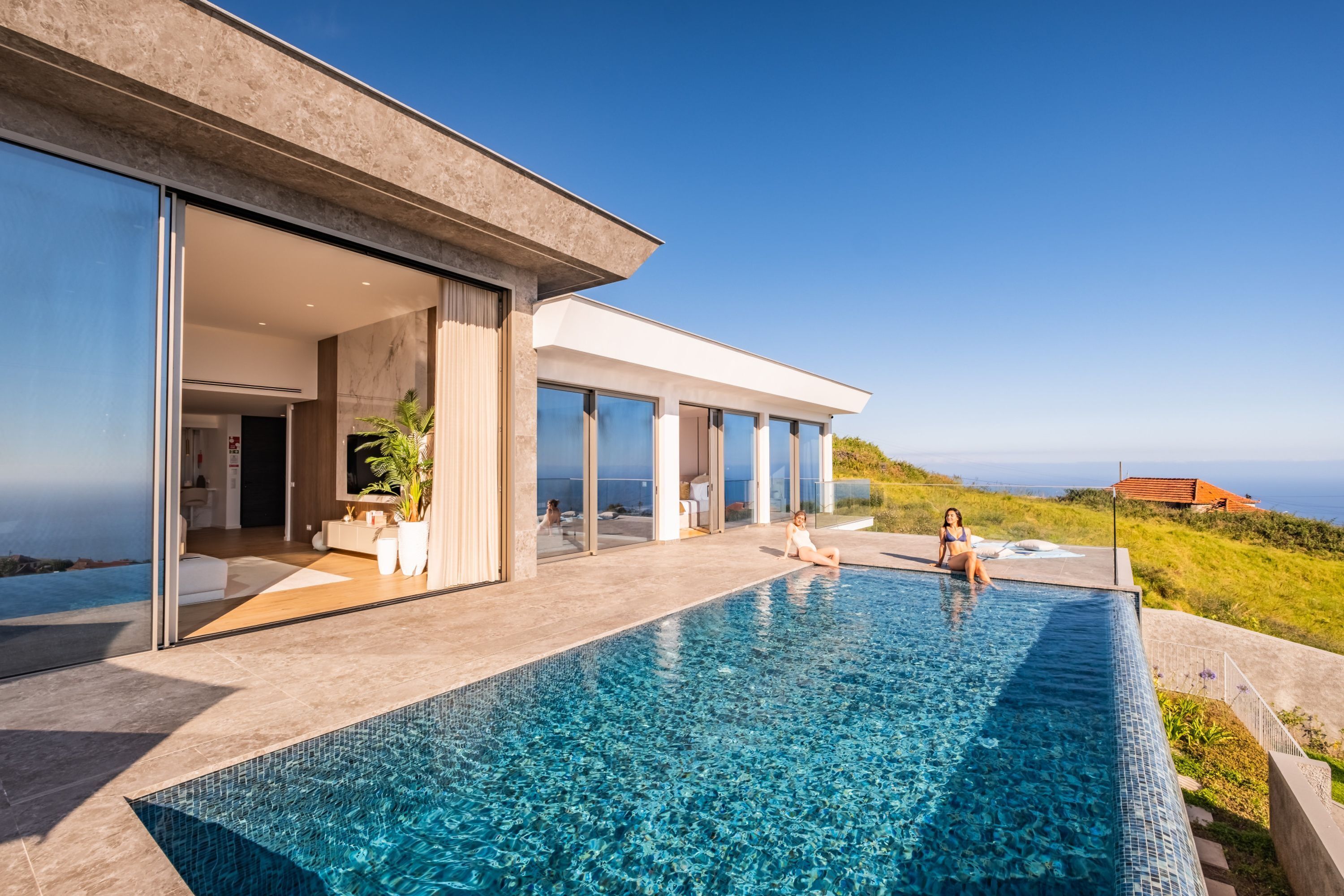 Una casa moderna con una gran piscina, un porche con paredes de vidrio y vista al océano.