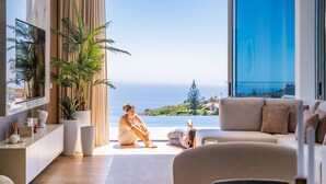 A modern living room with a large window overlooking a scenic view, a sofa, and a coffee table. - Villa Platinum by Homie (Calheta)