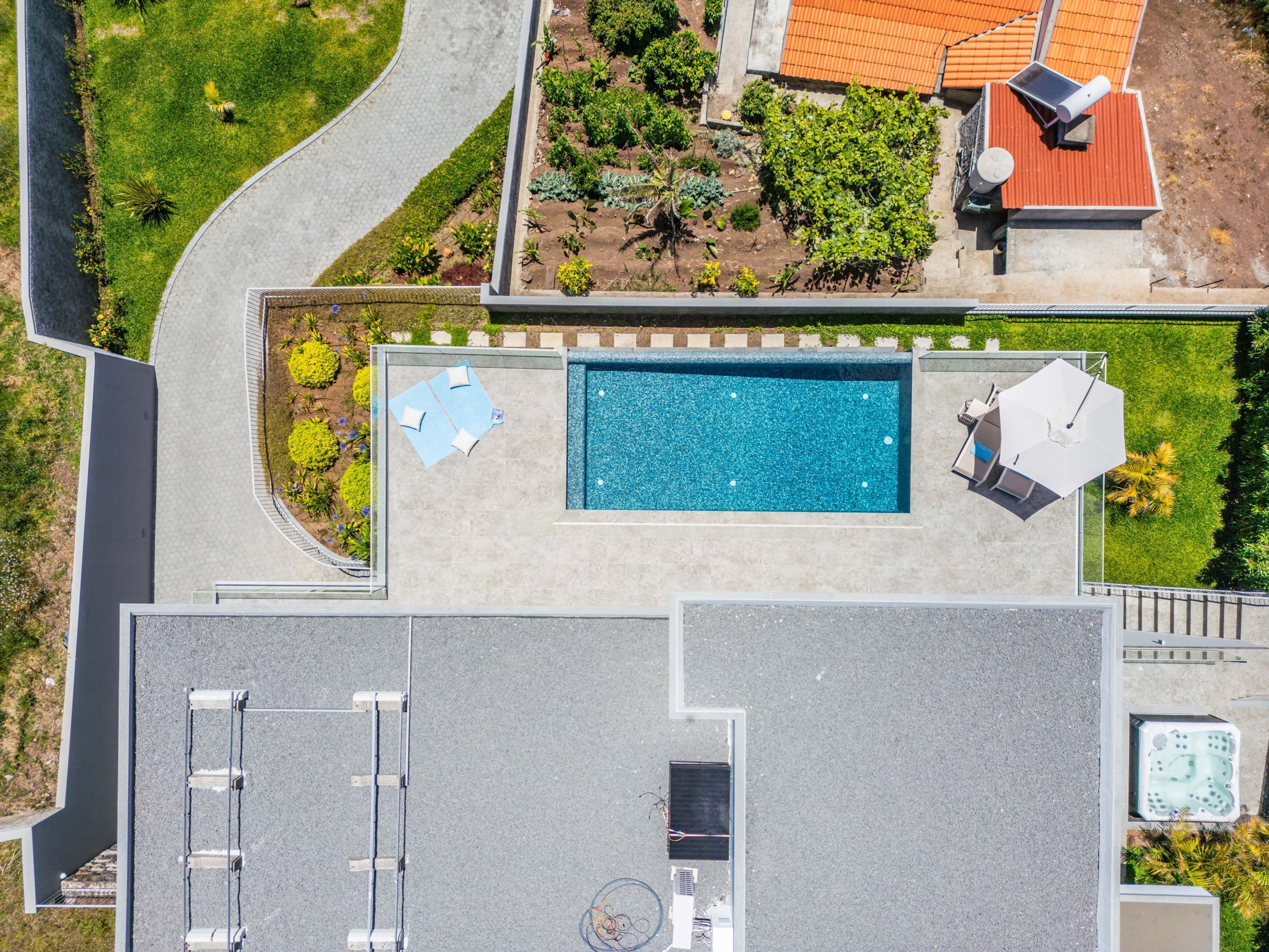 An aerial view of a residential property with a swimming pool, a covered patio, and a garden.