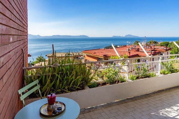 Ein Balkon mit Tisch, Blick auf das Meer und Gebäuden im Hintergrund.
