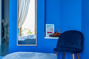 Ein Zimmer mit einem Bett, einem Sessel, einem Fenster mit Vorhängen, einem gerahmten Bild und einem Paar Schuhen auf einem Regal.