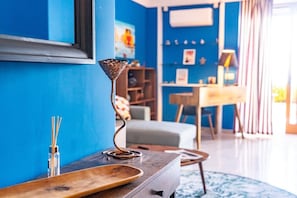 Ein modernes Wohnzimmer mit blauer Wand, einem Holztisch, einer Metallskulptur und einem Bücherregal.