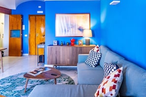 Ein modernes Wohnzimmer mit blauer Wand, grauem Sofa, Holzschrank und rundem Couchtisch.