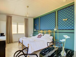 A bedroom with a bed, a desk, a chair, a vase with flowers, and a ceiling fan.