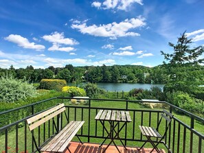 A deck with wooden benches and tables overlooking a lake, surrounded by greenery and trees.