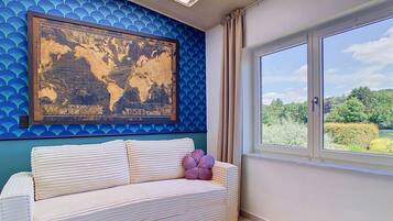 A room with a world map artwork, a sofa with cushions, a window with a view of greenery, and a skylight.