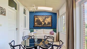 A dining area with a round glass table, black chairs, a world map on the wall, and a window with curtains.