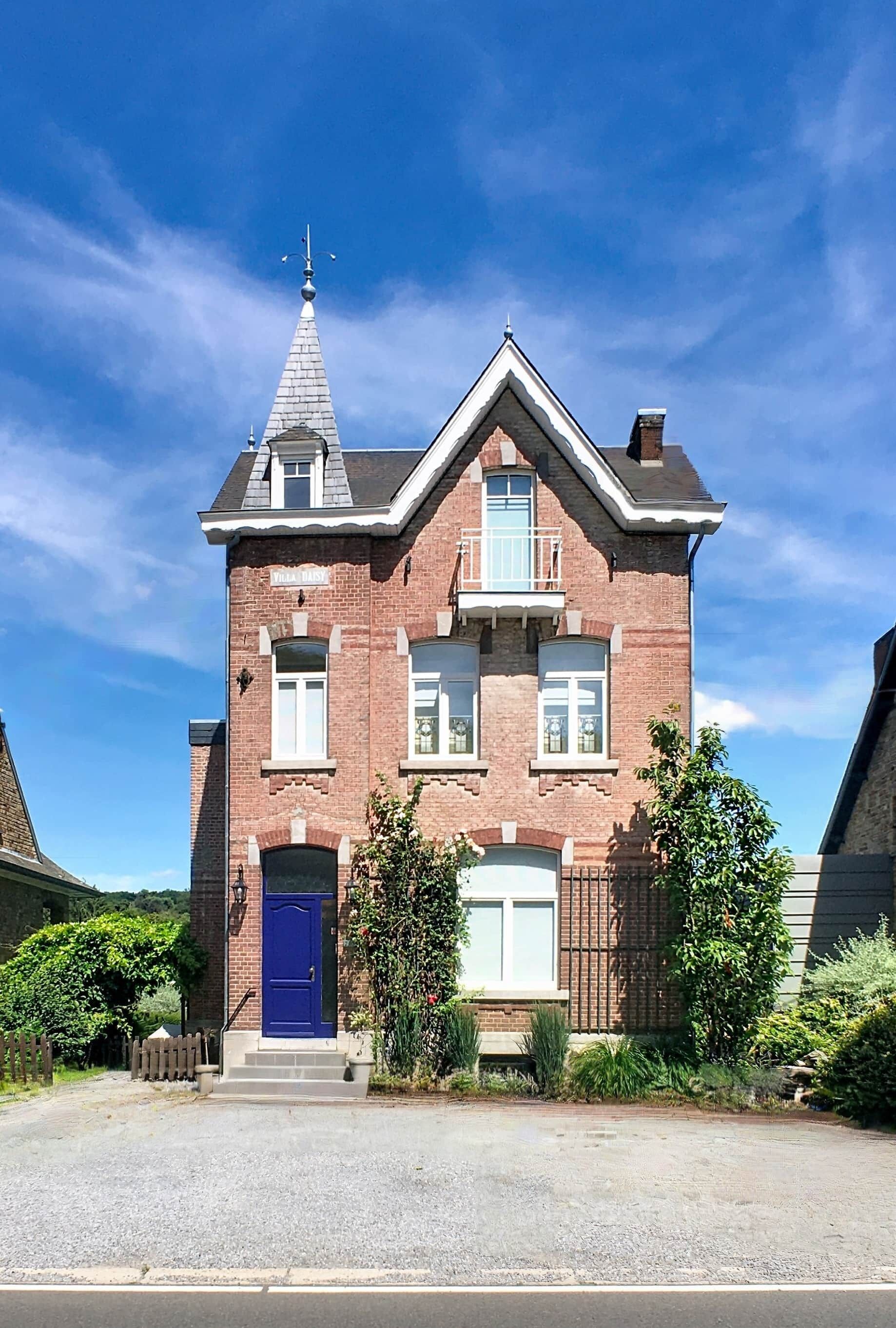Een tweelaags bakstenen huis met een blauwe deur, een klein balkon en een schoorsteen.