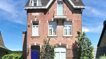 Een tweelaags bakstenen huis met een blauwe deur, een klein balkon en een schoorsteen.