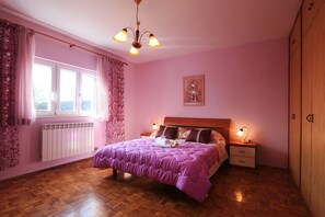Ein Schlafzimmer mit Bett, Nachttisch, Holzschrank, Fenster mit Vorhängen und einer Kristallleuchtre.