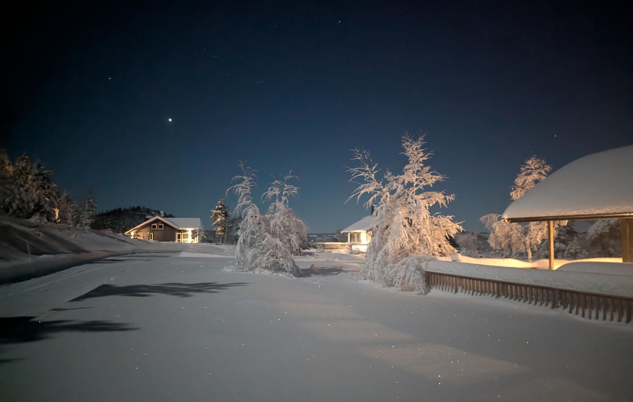 Un paysage enneigé avec une maison et des arbres, sous un ciel nocturne.