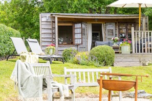 A rustic wooden cabin with a porch, outdoor seating, and a garden. - East Cornworthy Cottage (Totnes)