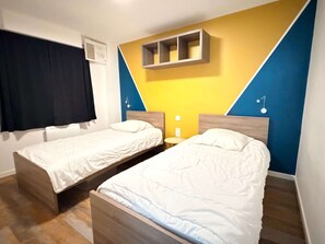 Ein Zimmer mit zwei Betten, einem Wandregal und einem Fenster mit Vorhängen.