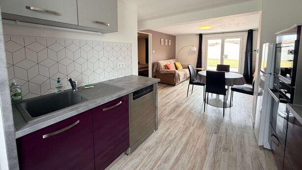 A modern kitchen with a dishwasher, a dining area with a table and chairs, and a living area with a sofa. - Oléron Honeysuckle (Saint-Georges-d'Oléron)
