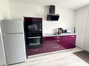 Eine kleine Küche mit Kühlschrank, Backofen, Mikrowelle und einer Kaffeemaschine auf der Arbeitsfläche.