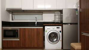 A compact kitchen with a microwave, washing machine, and refrigerator. - CityHouse TERA Emerald (Ho Chi Minh City)