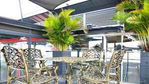 A glass-enclosed outdoor seating area with a metal table and chairs, surrounded by potted plants. - CityHouse TERA Emerald (Ho Chi Minh City)