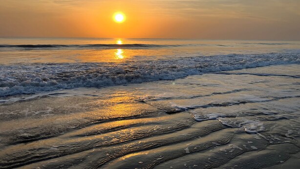 Une plage avec des vagues, un coucher de soleil et un ciel dégagé.