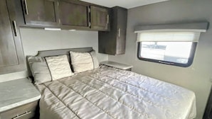 A bedroom with a bed, a window, and built-in cabinets. - Kenai River RV at Fish Camp + Processing (Soldotna)
